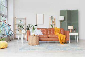 Modern living room interior with a brown leather sofa, yellow throw blanket, and a light blue bicycle by the window © Pixel-Shot