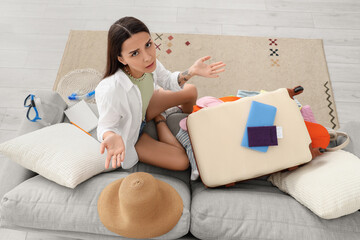 Confused young woman sitting on a sofa with an open suitcase, travel planning and packing problems, vacation preparation © Pixel-Shot