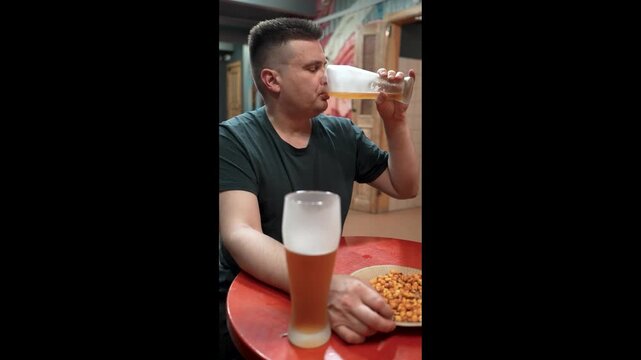 Young man holding a glass mug of light beer in a pub or bar. Close-up of a refreshing alcoholic drink with selective focus, social leisure, nightlife, relaxation and beverage concept.