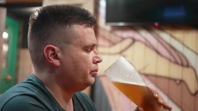 Young man holding a glass mug of light beer in a pub or bar. Close-up of a refreshing alcoholic drink with selective focus, social leisure, nightlife, relaxation and beverage concept.