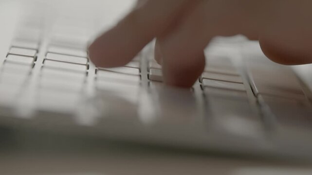 A close-up of fingers actively typing on a white Apple Magic Keyboard with soft minimal lighting in a clean workspace.