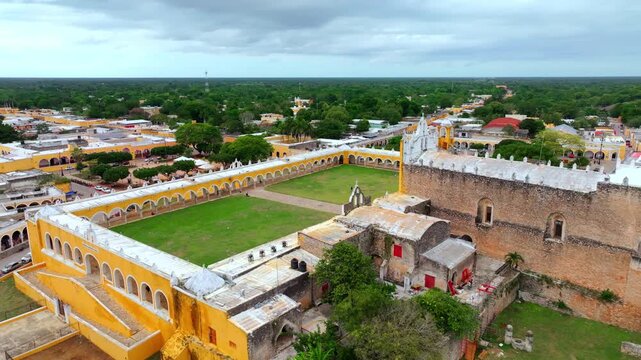 Aerial view of the huge green atrium and yellow arcades of the Convent of San Antonio de Padua in Izamal, Yucatan, Mexico, seen from above.