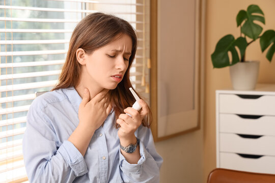 Young woman with sore throat holding a medical spray, Health problem and illness concept, home interior background