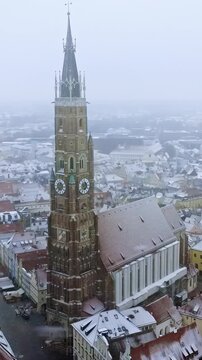 St Martin church tower aerial drone footage during winter snowfall in Landshut Germany medieval town.