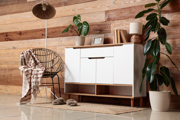 Obraz premium Cozy living room interior with wooden wall, modern white cabinet, rattan chair, and Green houseplants