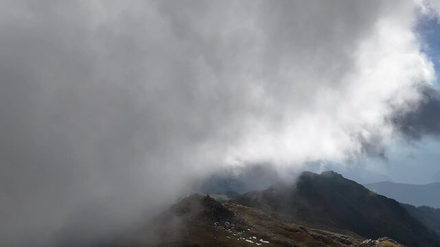 Cinematic 4K timelapse of mist and low clouds sweeping across a remote Himalayan mountain pass. Dramatic weather, rocky landscape, alpine terrain, and small snow patches create a moody wilderness atmo