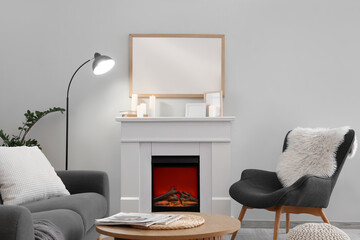 Obraz premium Cozy living room interior with a modern electric fireplace, comfortable gray sofa, and armchair with a fluffy pillow