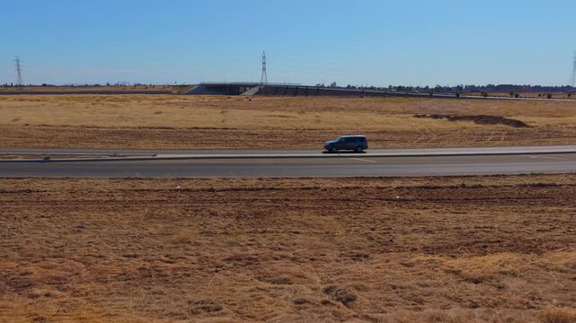 Low Altitude Reversing Aerial Drone Shot Over Dirt Field With Freeway Overpass Power Lines and Traffic in Fresno California