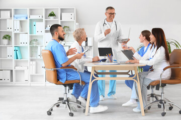 Fototapeta premium Male doctor working with laptop and his colleagues at table in clinic