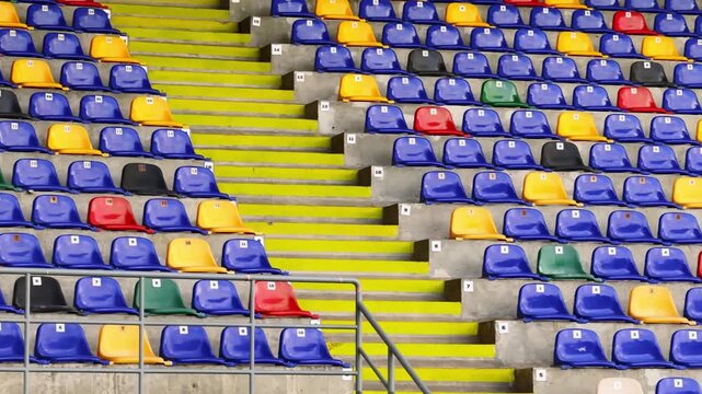 Empty stadium stands with colorful plastic seats, yellow stairs and concrete rows, showing sports venue seating and arena architecture.