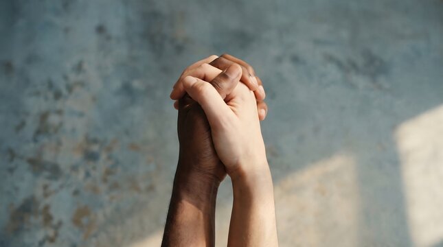 Close up of two people with different skin tones holding hands together in unity.