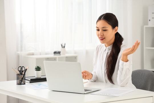 Young Asian businesswoman with modern laptop video chatting in office