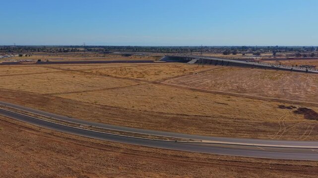 Reversing Arc Shot Aerial Drone Left to Right Over Dirt Field With Freeway Overpass Power Lines and Traffic in Fresno California