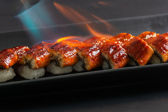 Chef Torching Unagi Sushi with Kitchen Blowtorch on Black Plate.
