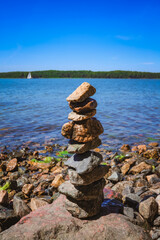 A picturesque coastal landscape featuring rocks stacked like a tower and blue sea water under a clear blue sky. Themes: Mediterranean nature, wild beach, geology, summer travel. © Vitalii