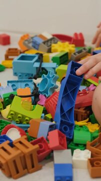 Vertical video. Two young children sitting on the floor surrounded by scattered colorful building blocks, sorting and connecting pieces together during playtime. Childhood creativity concept