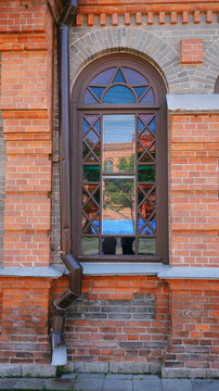 Elegant stone arched window with wooden frame and colored glass. Red stone wall, sunny day.