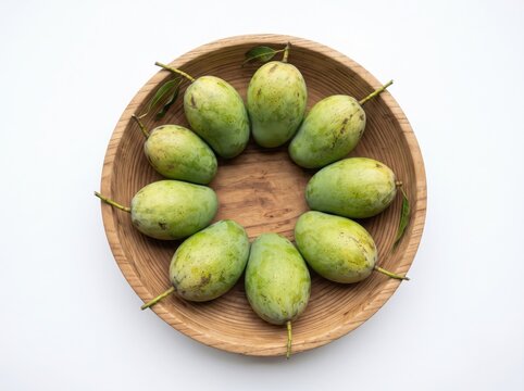 Raw green mangoes arranged in a wooden basket on white background space.