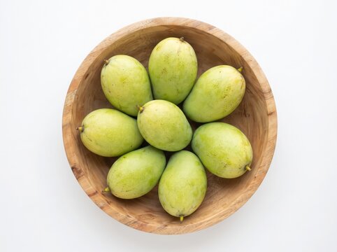 Fresh light green raw mangoes in a wooden bowl on white background top view.
