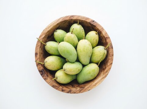 Fresh green mangoes in wooden bowl on white table top down view.
