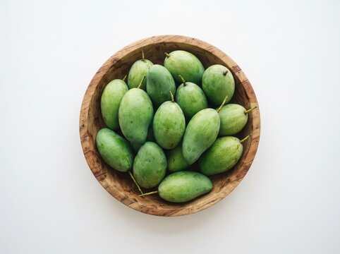 Fresh green mangoes in wooden bowl on white backdrop elevated view.