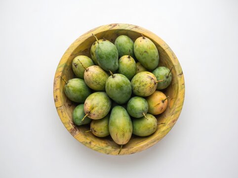 Fresh green mangoes in wooden bowl overhead view on white background.