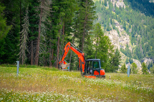 Mini excavator working in an alpine meadow surrounded by forest in the Dolomites, Italy