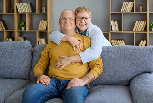 Seniors couple grandparents embrace hugging at home. They relax on a sofa in a living room, smiling and hugging, showing togetherness, trust and love in retirement. Concept of love and trust.