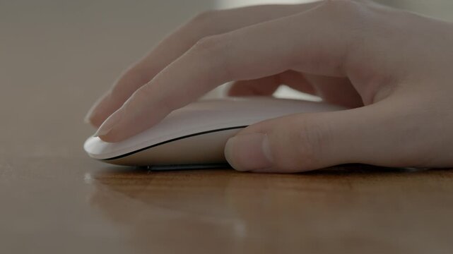 A close-up of a woman's hand using a dark ergonomic wireless mouse on a desk surface in a professional workspace.