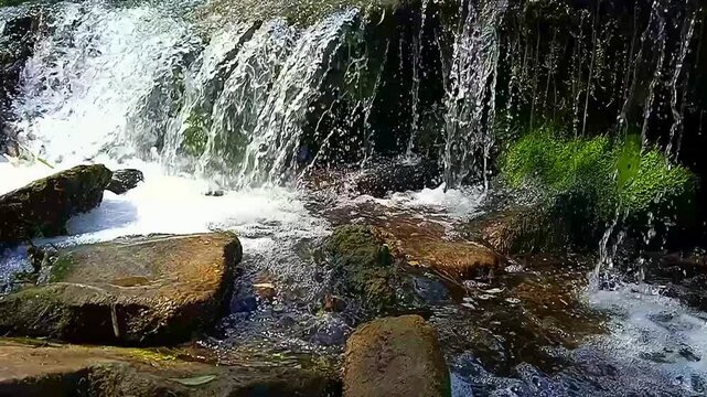 Natural waterfall cascading over mossy rocks, fresh mountain stream flowing through forest stones, serene river water motion in wild nature
