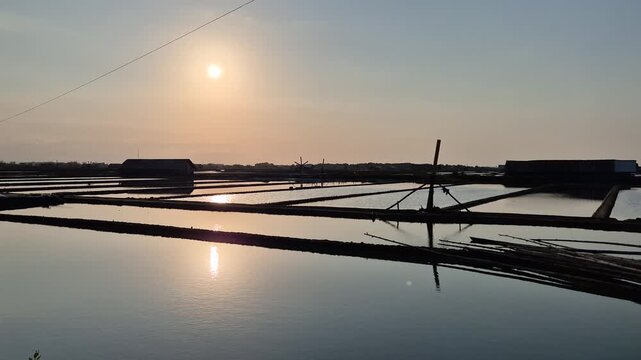 Sunrise Reflection on Traditional Salt Pans with Wooden Windmill