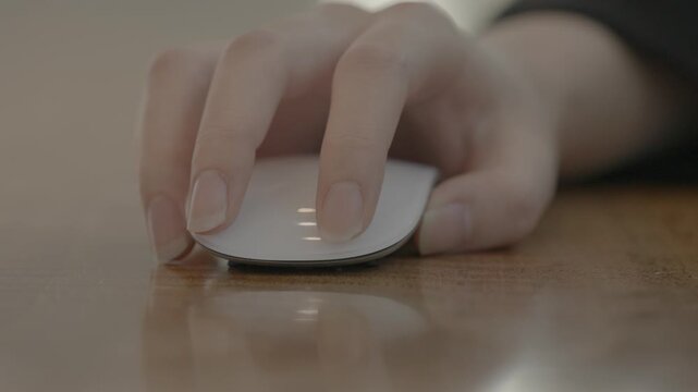 A close-up of a woman's hand using a dark ergonomic wireless mouse on a desk surface in a professional workspace.