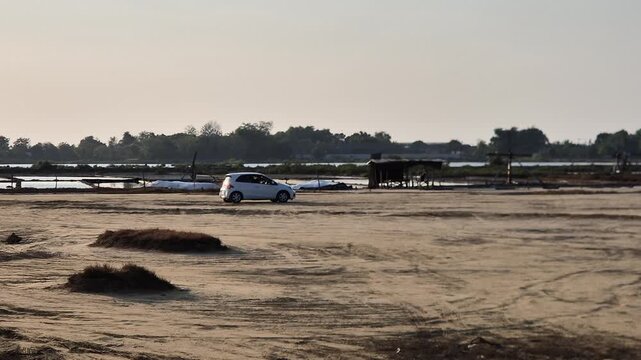 A white hatchback moves slowly across a dry, dusty field near the salt pans as someone practices driving.