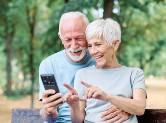 Obraz premium Happy active senior couple having fun using smartphone and wearing sportswear, checking music or an exercise app, after having an exercise sport activity outdoors