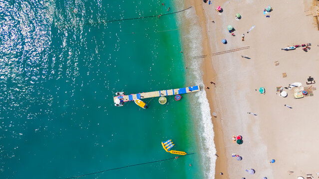 Oludeniz, Turkey. Aerial top down view of Oludeniz Beach with rows of umbrellas, crowded pebble shore, sea waves and pontoon pier in turquoise water, summer.. Aerial View