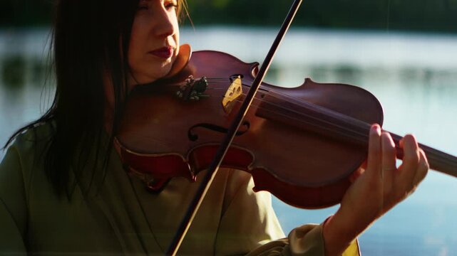 Focused violinist playing a classical melody outdoors by a tranquil lakeside, illuminated by soft natural sunlight with calm water and distant greenery in the background