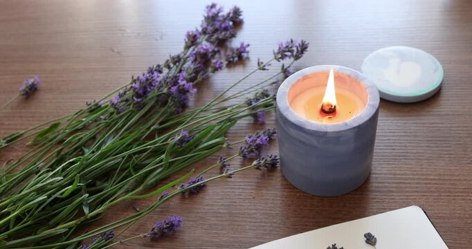 Handmade concrete candle burning on wooden table background. Modern lavender aromatherapy product design for home decor. Craft violet candle holder with beautiful flame video.