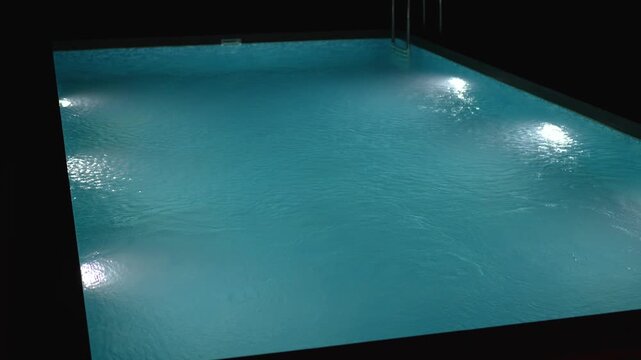 Swimming pool with clear blue water and bright underwater lights at night.