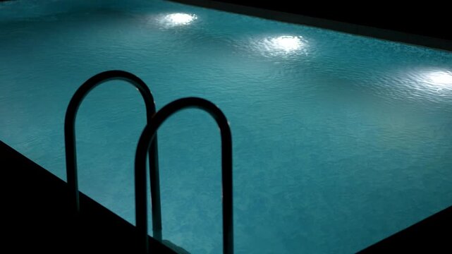 Swimming pool with clear blue water and bright underwater lights at night.