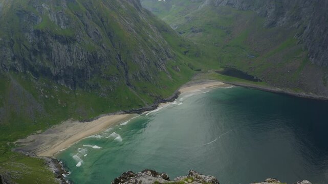 Kvalvika Beach curves below steep rock walls as small waves break onto pale sand inside a sheltered bay viewed from Ryten.