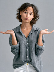 Naklejka premium Young woman shrugging hands, casual gray shirt, white pants, neutral background, uncertain expression, short brown hair, studio portrait