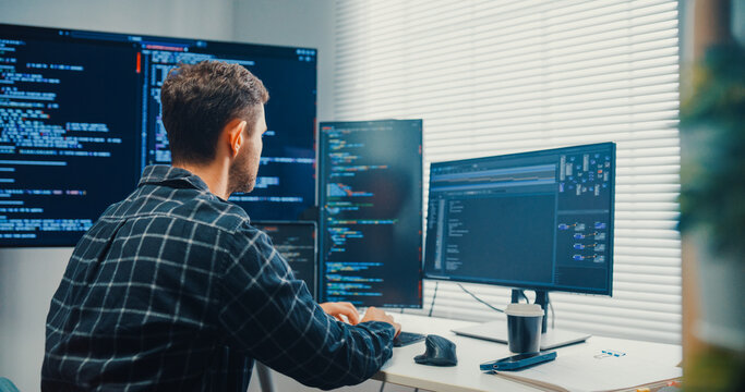 Young Caucasian male programmer writes code using multiple screens in home office workspace. AI development, cybersecurity, network database system, software engineering, remote tech startup concept.