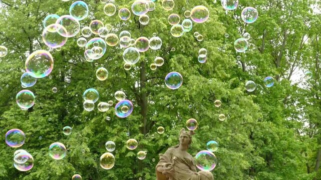 
A multitude of colorful soap bubbles flying through the air against a backdrop of park trees. Children's recreation and entertainment.
