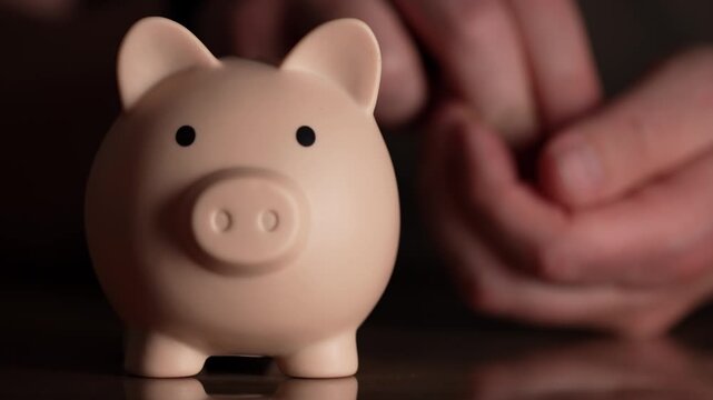 A charming pink piggy bank rests on a dark, reflective surface, symbolizing the careful act of saving. Soft hands hover in the background, safeguarding a growing nest egg for future endeavors.