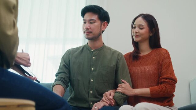 Asian female financial advisor discuss showing tablet to young couple on sofa in living room at home. Insurance consultation plan, house estate mortgage loan meeting, corporate banking broker concept.