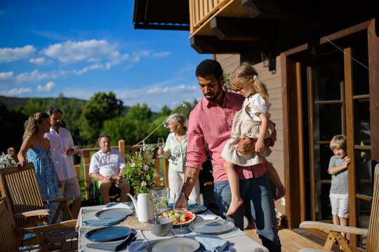 Family with kids preparing barbecue party dinner on patio, people sitting at table on patio and talking