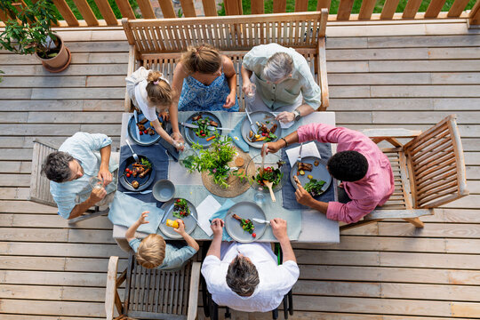 Above shot of family eating at barbecue party dinner on patio, little girl eating roasted corn and enjoying it.