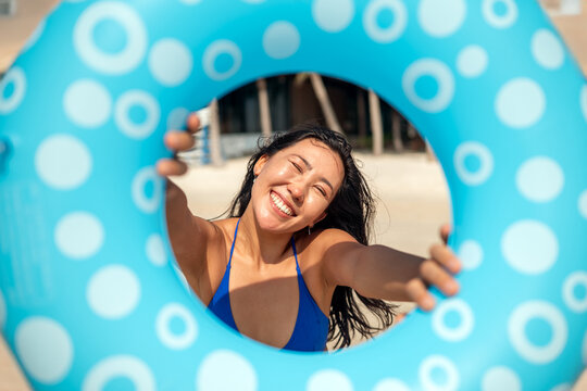 Happy young woman laughing through a blue inflatable ring on a tropical beach, summer vacation