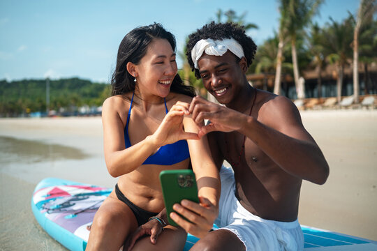 Young multiethnic people, couple having fun on surfboards in the clear ocean water during summer