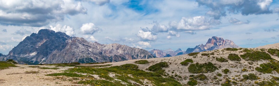 Vast mountain panorama with massive limestone peaks and vegetated high plateau under a cloudy sky in the Dolomites, Italy
